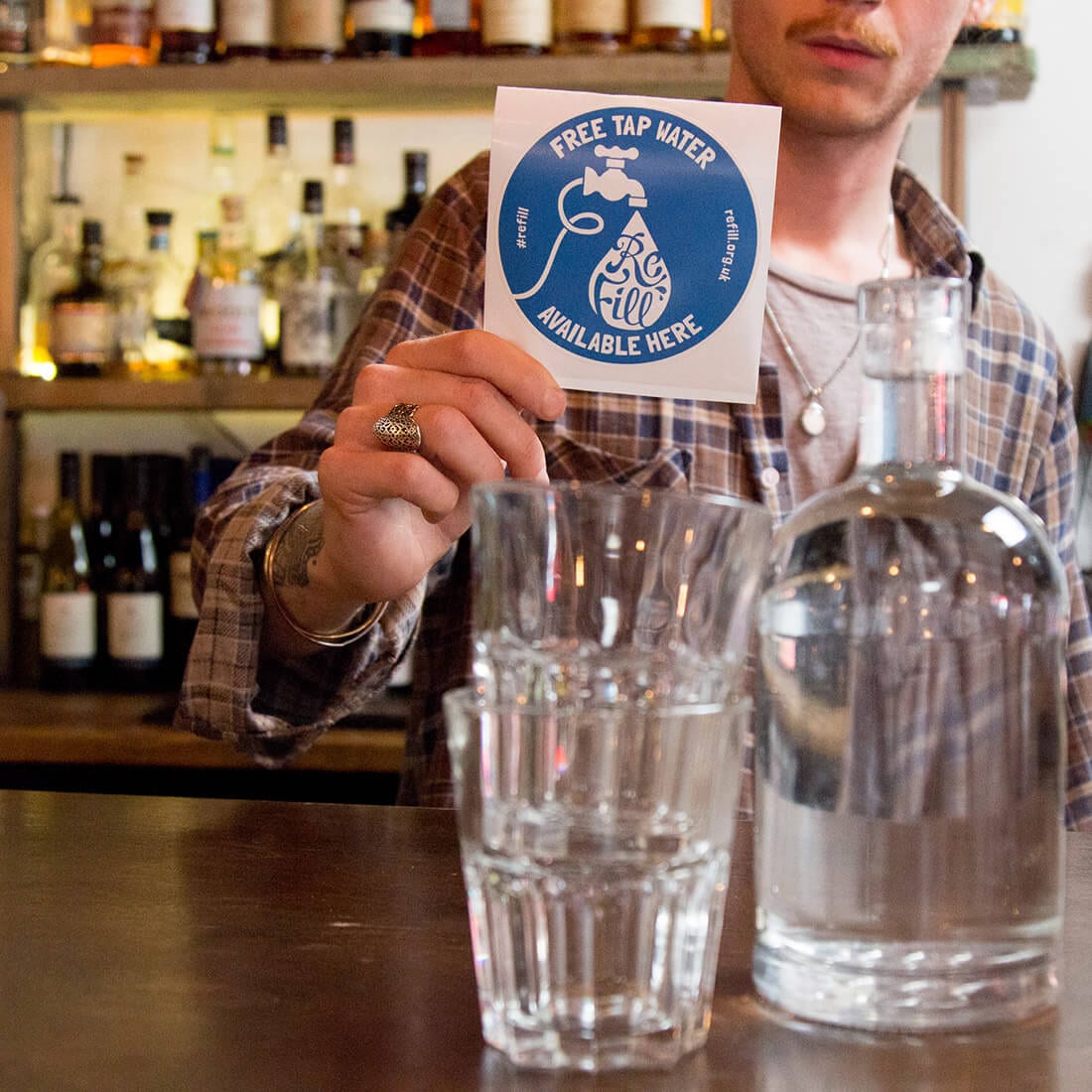 man in bar with Refill sticker and two glasses with a bottle of water